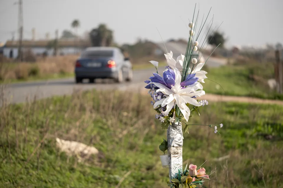 A bouquet of flowers stands in the grass beside a rural road as a car drives by.